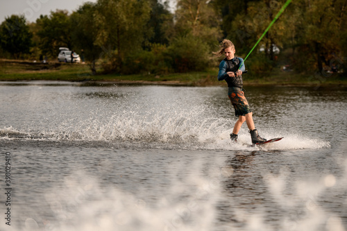 view on young man in wetsuit and vest riding wakeboard on the river