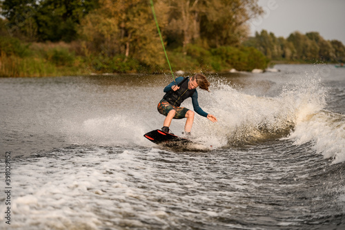 handsome young man stands with bent knees on wakeboard and ride down on wave