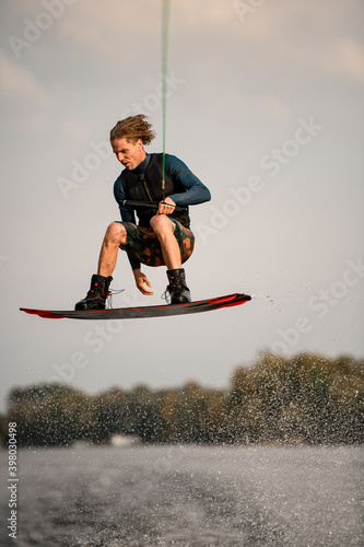 active male wakeboarder in wetsuit jumping high over river water