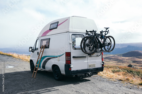 Amazing vintage camper van parked on gravel wild camping spot. Two bikes attached to bike rack in the back. Sleeping on top of car. Vanlife adventures concept