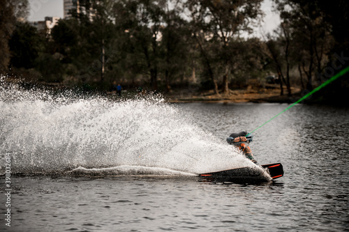 Athletic man in vest balances on wakeboard on the water holding hands on cable © fesenko