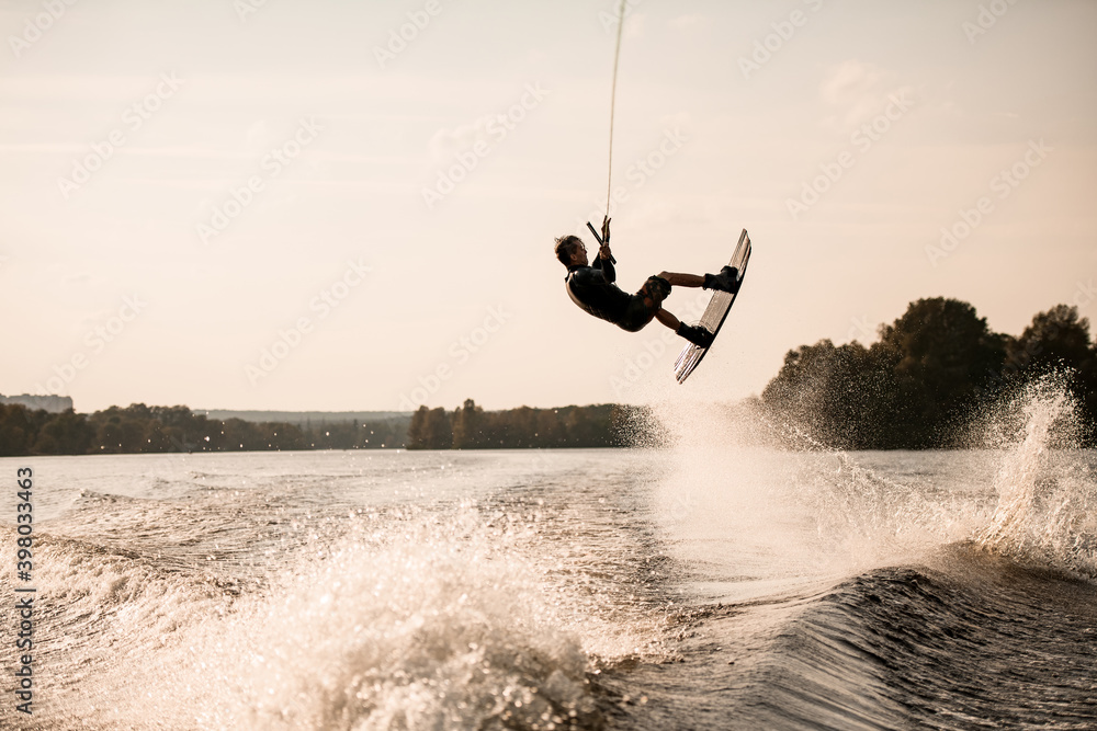 view on energetic muscular man holding rope and masterfully makes flips with wakeboard over splashing water
