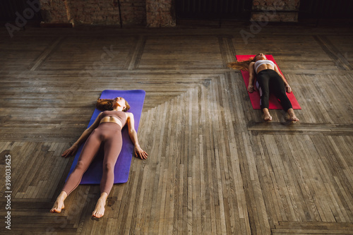 Two young women do complex of stretching yoga asanas in loft style class. Shavasana. photo