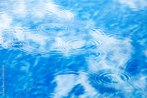 Raindrops on pool blue water surface. Blue water texture as background. Stains circles on the water from rain