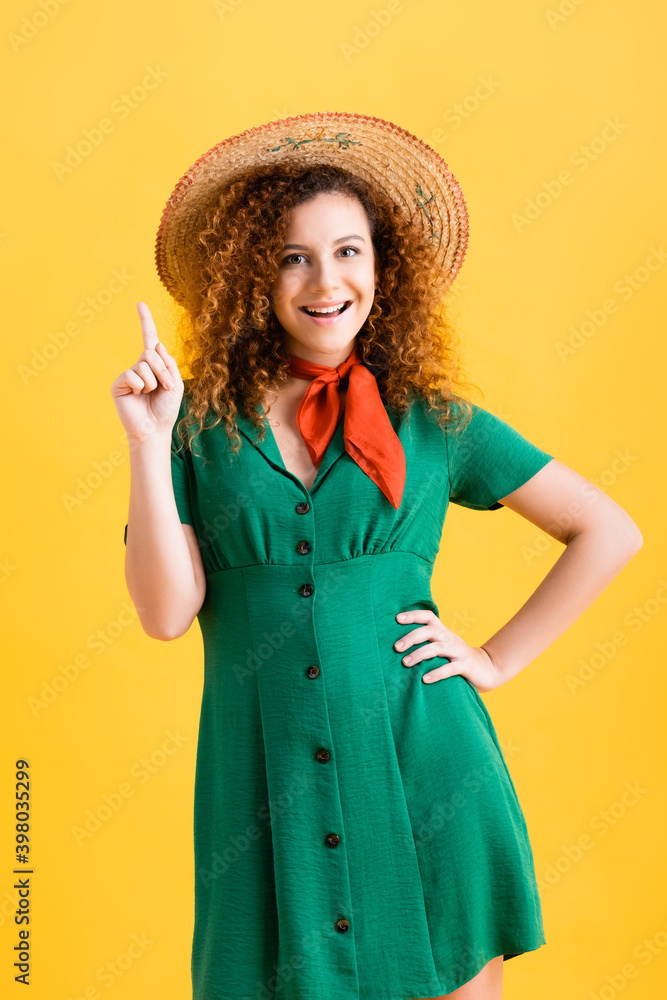 happy young woman in straw hat and green dress pointing with finger on yellow happy young woman in straw hat and green dress pointing with finger on yellow