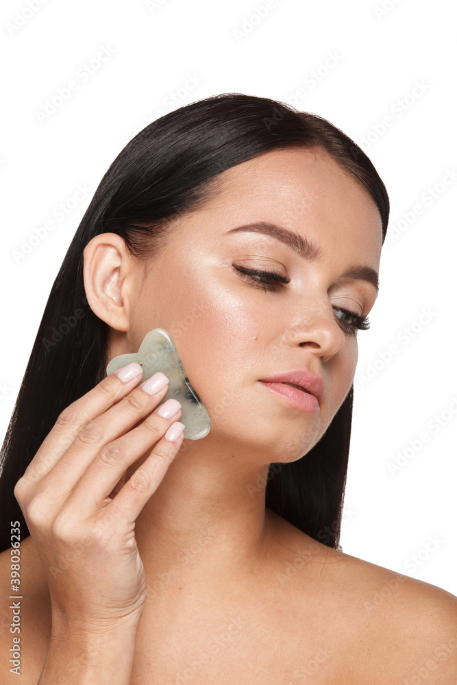 Beautiful girl with natural makeup and clean skin. Holds in hand a jade face scrubber for slimming anti aging wrinkles. Massage instrument for body skin care. Detox facial massager