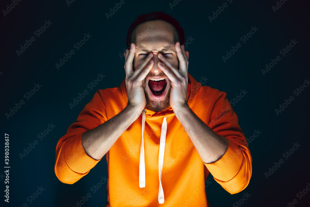 Hiding face. Portrait of crazy scared and shocked caucasian man isolated on dark background. Copyspace for ad. Bright facial expression, human emotions concept. Watching horror on TV, cinema. Hiding face. Portrait of crazy scared and shocked caucasian man isolated on dark background. Copyspace for ad. Bright facial expression, human emotions concept. Watching horror on TV, cinema.
