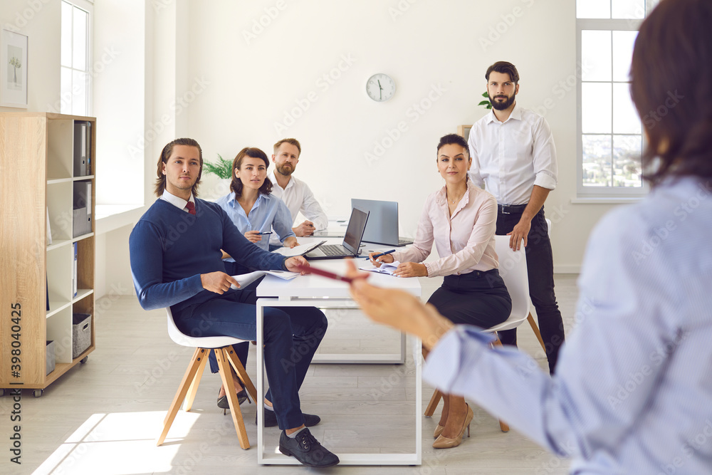 Group of office workers sitting and listening to colleague making presentation in office