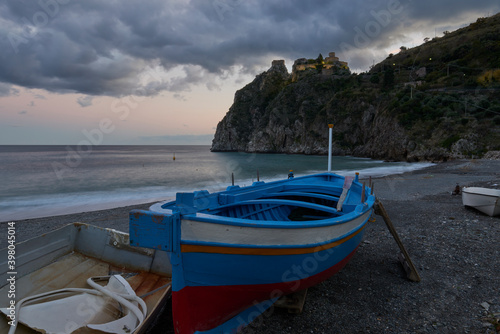 A typical wooden fishing boat at the beach under the illuminated Rocca, near Taormina in long exposure.