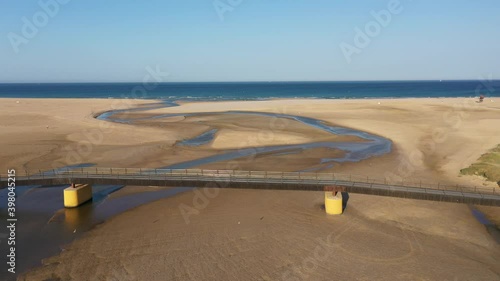 Aerial views of bridge over Rio Salado river in Conil de la frontera with water flowing through the beach into the Atlantic ocean seen from above