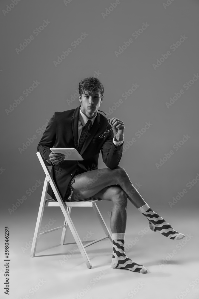 Fototapeta premium Devices. Young fashionable, stylish man wearing jacket and socks working from home. Fashion during insulation 'cause of coronavirus pandemic. Half business and half home style. Black and white.