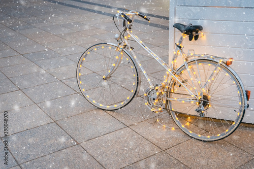White retro bicycle with Christmas lights during falling snow