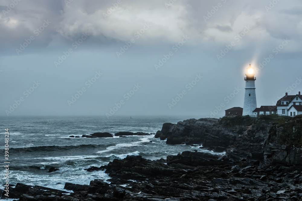 Gloomy gloomy photo of a luminous lighthouse on a rocky shore. Famous lighthouse. Portland. USA. Maine