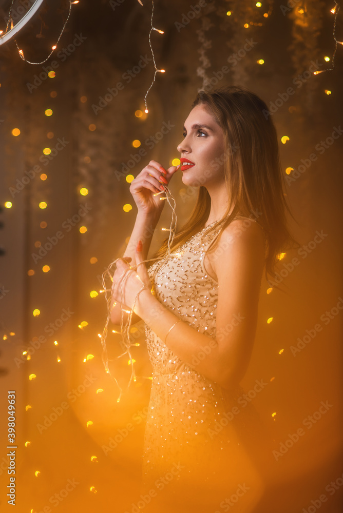 Elegant woman in evening beige fashion dress in golden christmas decorations. Bokeh lidgts and snowy new year decorated arch. Magic miracle surround