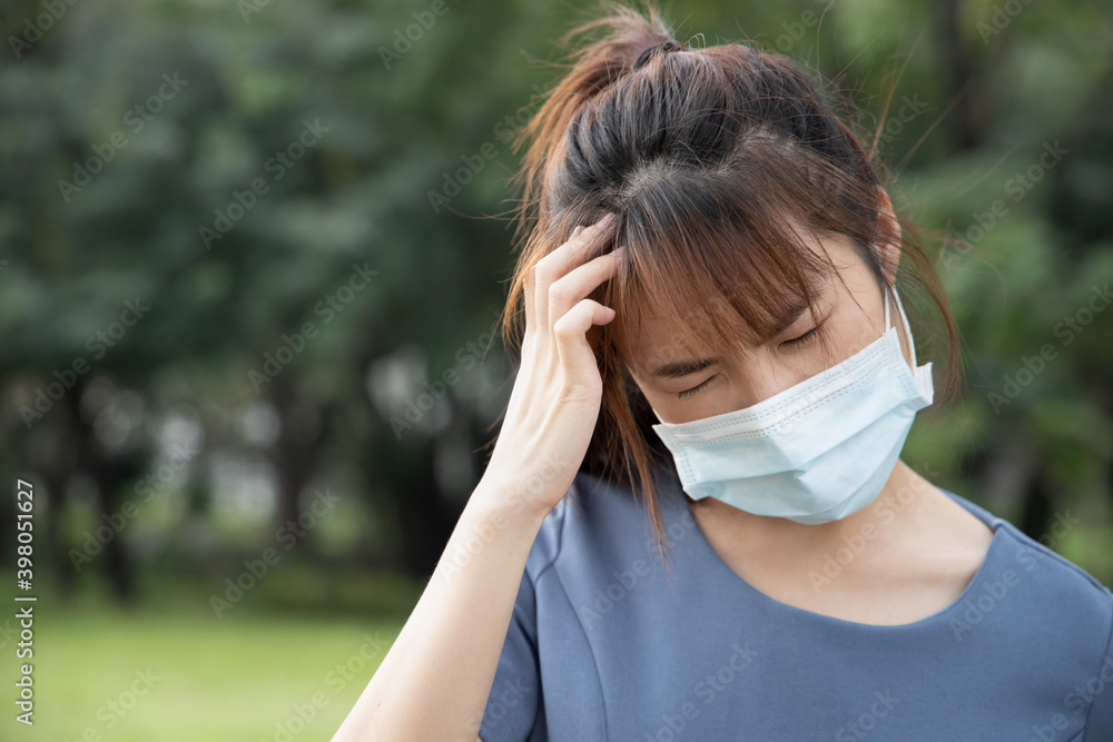 Asian woman having headache fever, wearing face mask in outdoor park, concept of coronavirus infection, social distancing, new normal lifestyle while waiting for coronavirus cure, COVID-19 vaccine Asian woman having headache fever, wearing face mask in outdoor park, concept of coronavirus infection, social distancing, new normal lifestyle while waiting for coronavirus cure, COVID-19 vaccine