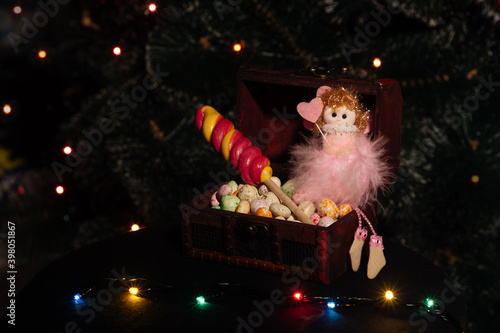 Wood Box with assorted delicious candy and toy for New Year and Christmas. New Year's sweets and pink fairy on a dark background. New Year's concept
