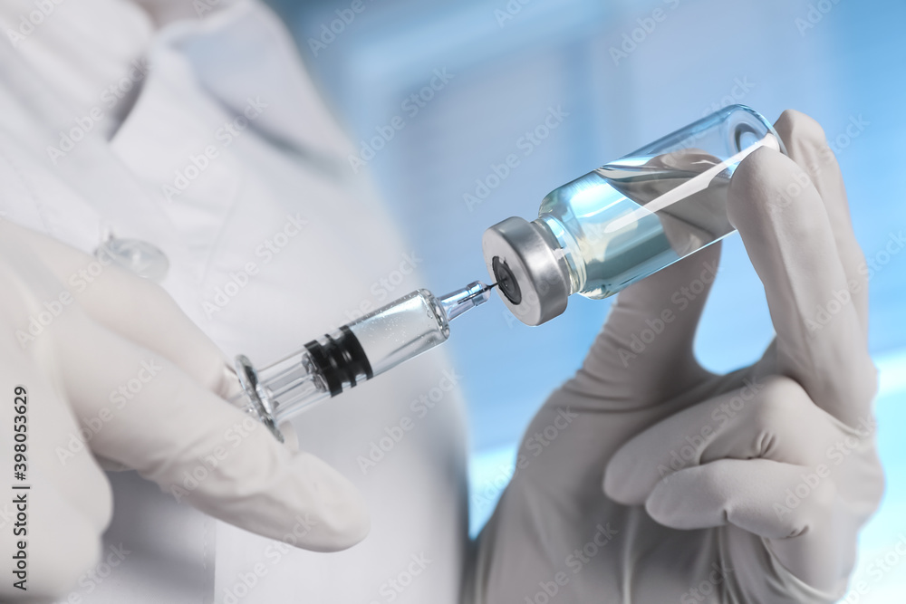 Doctor filling syringe with vaccine from vial on blurred background, closeup Doctor filling syringe with vaccine from vial on blurred background, closeup