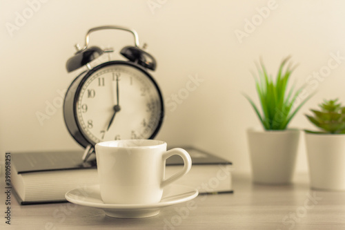 A small Cup of morning coffee, an alarm clock, and a book on the table.