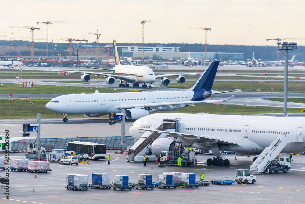Busy airfield view with airplanes and service vehicles. View of International Airport with planes, gangways, trucks and service equipment. Travel and industry concepts. - obrazy, fototapety, plakaty 