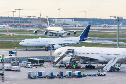 Busy airfield view with airplanes and service vehicles. View of International Airport with planes, gangways, trucks and service equipment. Travel and industry concepts.