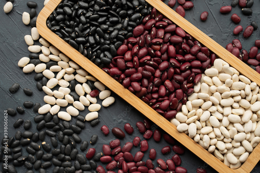 beans in bamboo plate. bowl of beans. black bean, red kidney bean and white bean. navy bean, cannellini bean, white kidney bean on dark gray background and scattered various beans