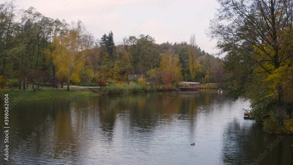 Beautiful autumn park with bridge over lake from aerial view. Slow drone flight over water surface. Beautiful autumn park with bridge over lake from aerial view. Slow drone flight over water surface.