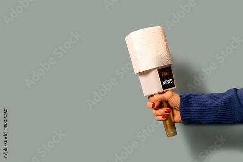 on a blue background, a journalist's microphone, instead of a sound filter, is wearing a roll of toilet paper. the caption on the microphone is Fake news.The concept of an unfair press.