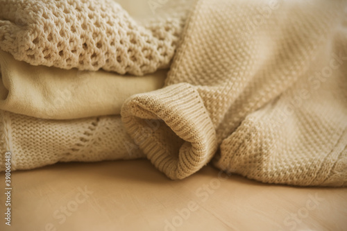 Beige wool warm sweaters lie on the bed, folded in a pile, from which the sleeve of one of the sweaters has fallen. Warm clothing for cold autumn and winter.