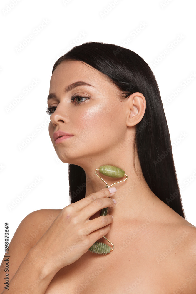 Beautiful young woman with perfect skin wearing towel on head using a jade face roller with natural quartz stones on white background Beautiful young woman with perfect skin wearing towel on head using a jade face roller with natural quartz stones on white background