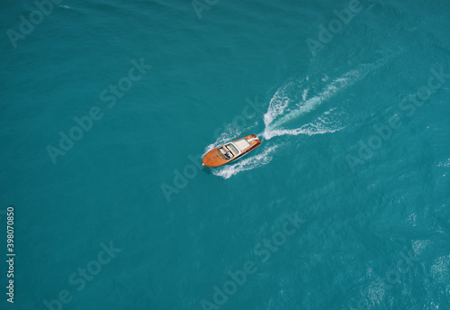 Wooden runabout in the rays of the sun on turquoise water. Drone view of a boat  the blue clear waters. Top view of a wooden boat sailing to the blue sea. Classic Italian motorboat.