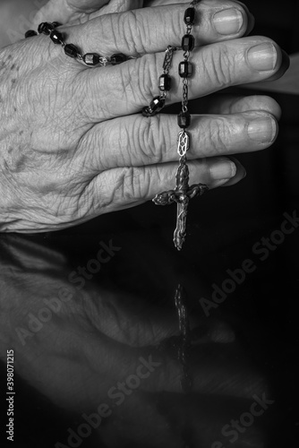 Faith, lady's hands with a third praying over black reflective surface, selective focus.