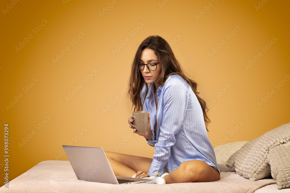 Attractive young woman in blue shirt, wearing glasses, sitting at her computer, holding a cup of tea in her hands Attractive young woman in blue shirt, wearing glasses, sitting at her computer, holding a cup of tea in her hands