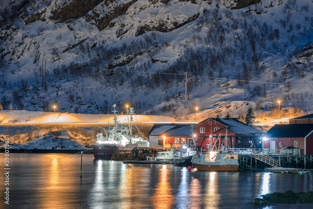 Fishing boat anchored at dock in illuminated fishing village on coastline at Lofoten Islands
