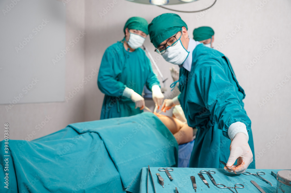 Team surgeon choosing scalpel while operating seriously injured patient in operating room Team surgeon choosing scalpel while operating seriously injured patient in operating room