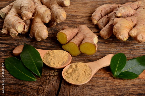 Fresh ginger root and ginger powder in the wooden spoon on a old wooden background. Green leaves