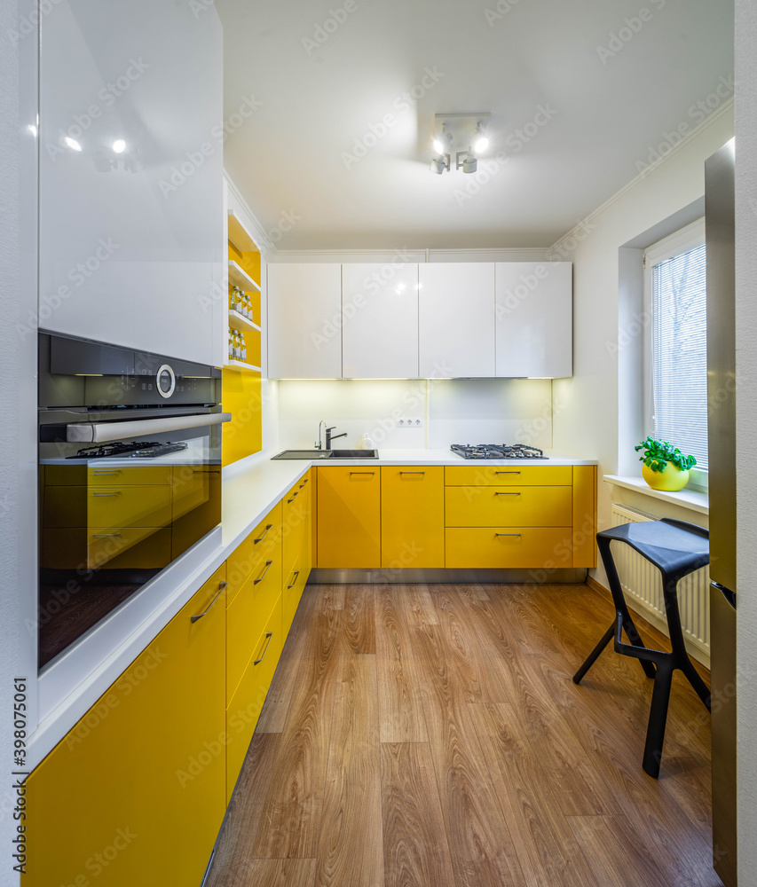 Fototapeta premium Modern interior of kitchen in luxury apartment. Yellow kitchen set with white counter. Black sink. Gas stove. Oven. Cabinets and drawers.