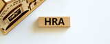 House Rent Allowance symbol. Wooden block with word 'HRA, House Rent Allowance' near miniature house. Beautiful white background, copy space. Business and HRA concept.