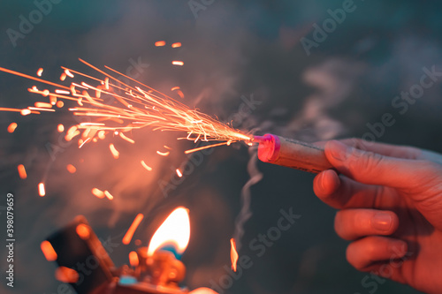 Young Man Lighting Up Firecracker in his Hand Using Gasoline Lighter. Guy Getting Ready for New Year Fun with Fireworks or Pyrotechnic Products - CloseUp Shot, Rear View photo