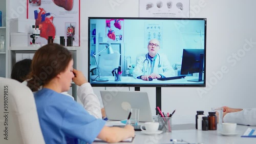 Concentrated purposeful experienced medical team holding online video meeting with senior doctor on interactive screen. Team of specialists discussing diagnosis of patients uing video conference photo