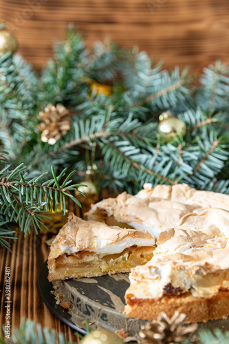 gedeckter Kuchen mit Apfel und Marzipan mit einer Haube aus Baiser auf einem Tisch aus Holz zur Weihnachtszeit mit Zweigen von der Tanne oder einem Nadelbaum