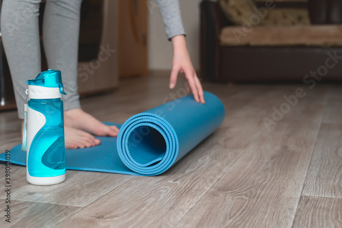 Teenage girl doing fitness exercise, practicing yoga at home. Healthy lifestyle concept. She spreads the yoga mat. Workout at home. Home interior, daytime.