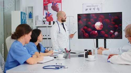 Doctor presenting virus development on digital screen in front of colleagues pointing on monitor in hospital office during brainstorming. Team of physicians analysing diagnosis of patients photo