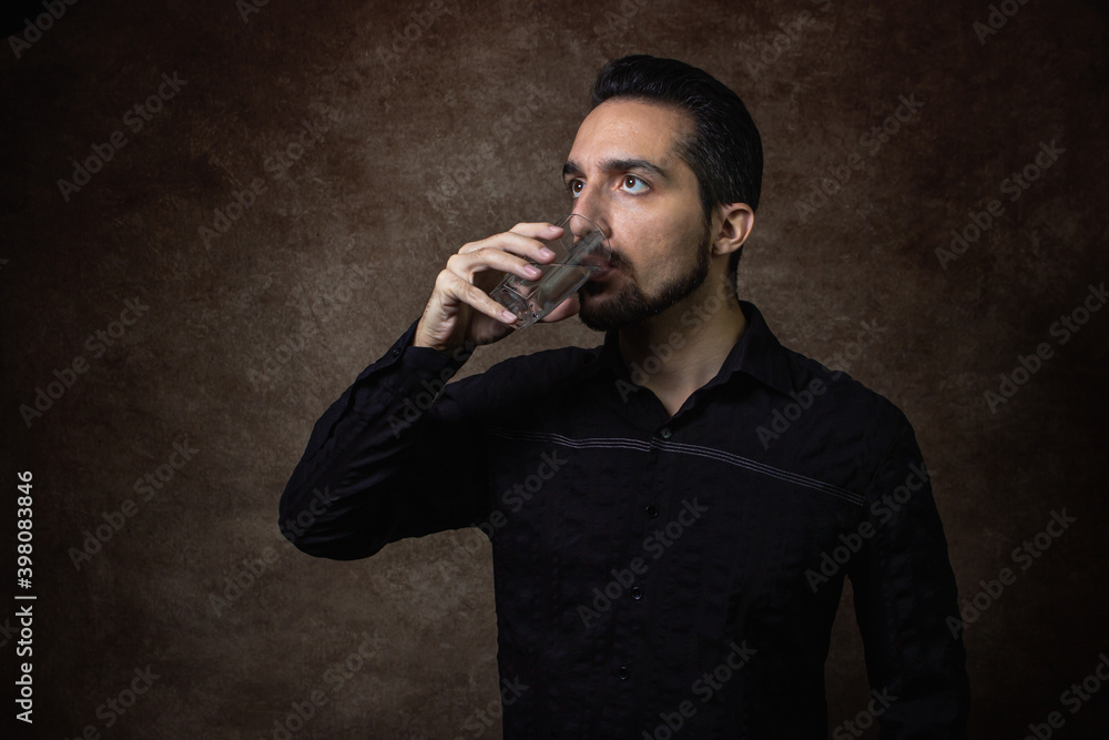 Portrait of a man. The guy drinks water. Portrait on a brown background. Guy in a black shirt