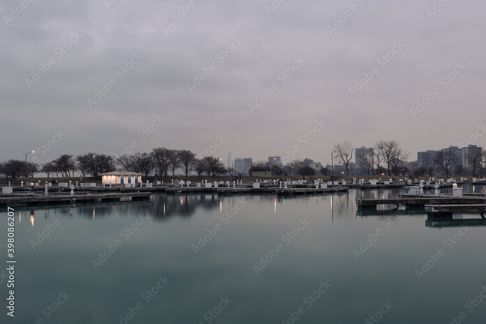 Well lit boat house behind empty docks on calm water with overcast sky in Chicago