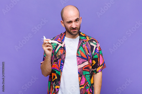 фотографія young bald man feeling puzzled and confused, with a dumb, stunned expression loo