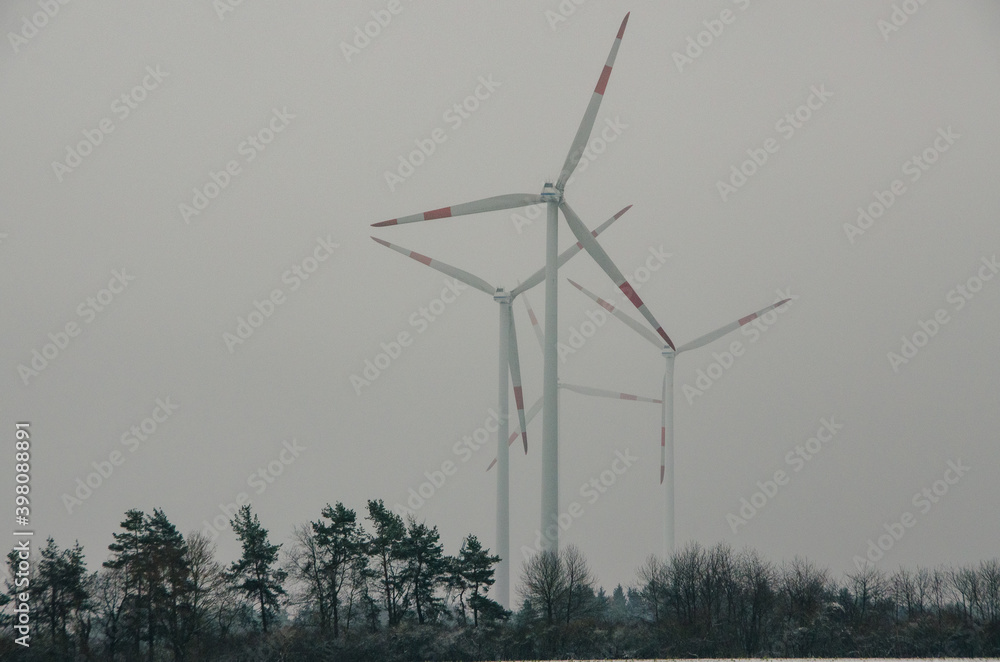 Several wind turbines in front of grey autumn sky, forest in the foreground. High quality photo Several wind turbines in front of grey autumn sky, forest in the foreground. High quality photo