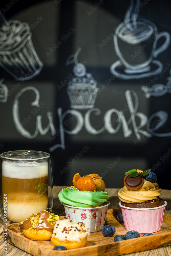 Cupcakes with fruits and berries and coffee on a wooden table, a wall with chalk drawings, different light effects.