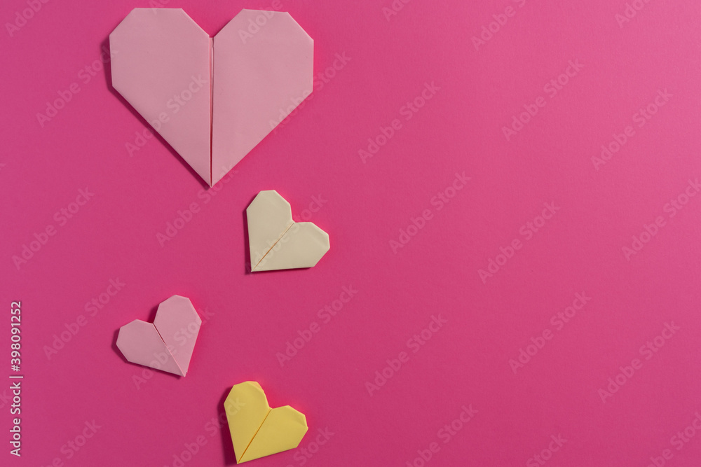 Origami hearts made with colored paper for congratulations on Valentine's Day for couples in love, on pink background