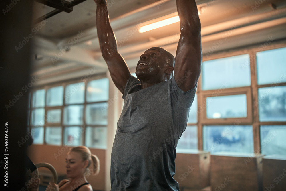 Fototapeta premium Fit man sweating while doing pull-ups at the gym