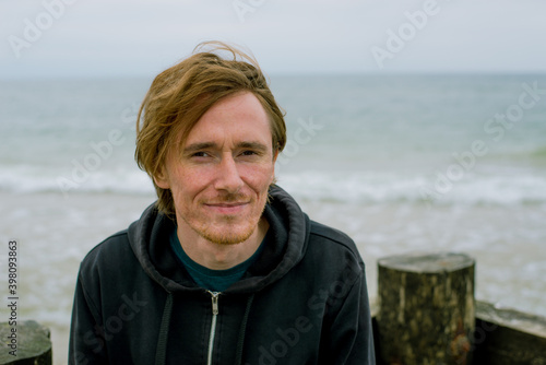 a young man, Caucasian,  looks at the camera by the sea
